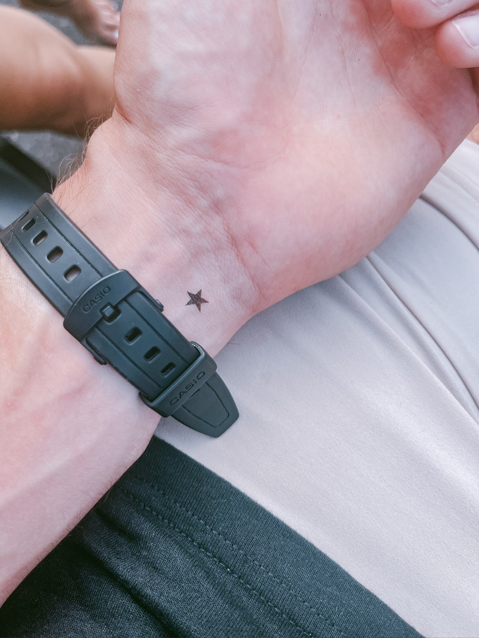 Close-up of a wrist with a black watch strap and a small star tattoo.