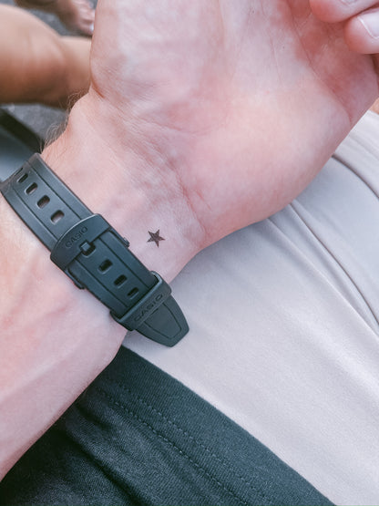 Close-up of a wrist with a black watch strap and a small star tattoo.